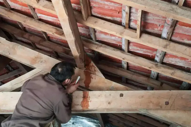 Artisan intervenant sur les poutres d’une charpente traditionnelle en bois.